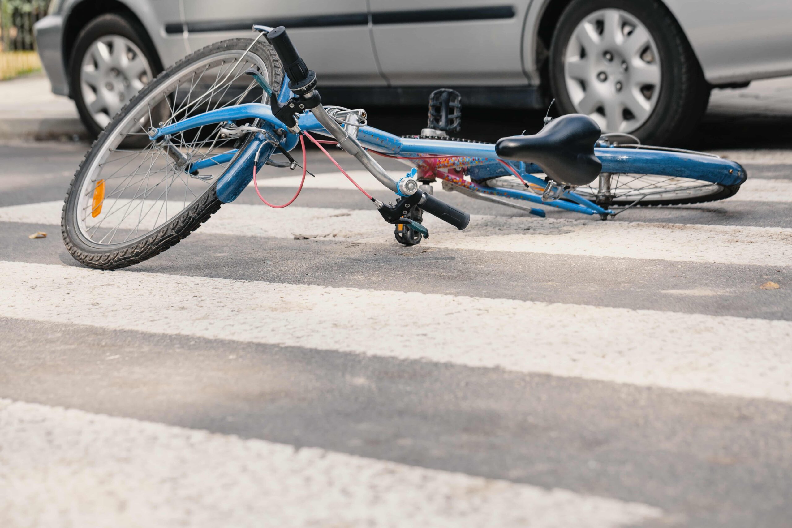 Bicycle lying on a crosswalk in front of a car, representing a bicycle accident or cyclist involved in a road collision.