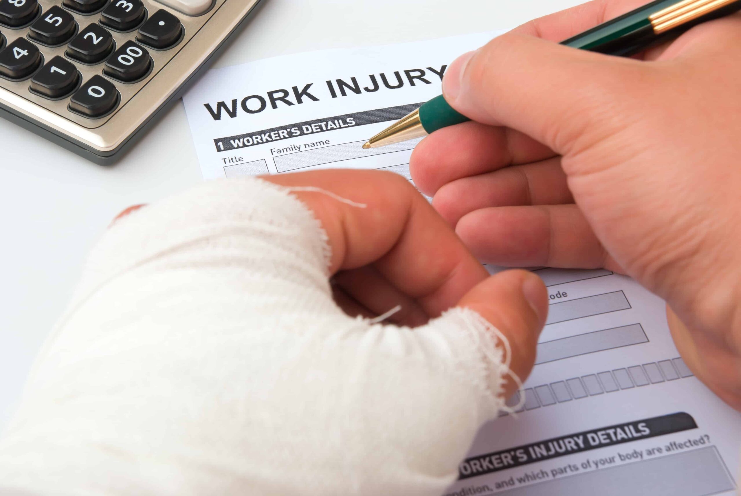 Injured worker with bandaged hand filling out a work injury claim form at a desk.