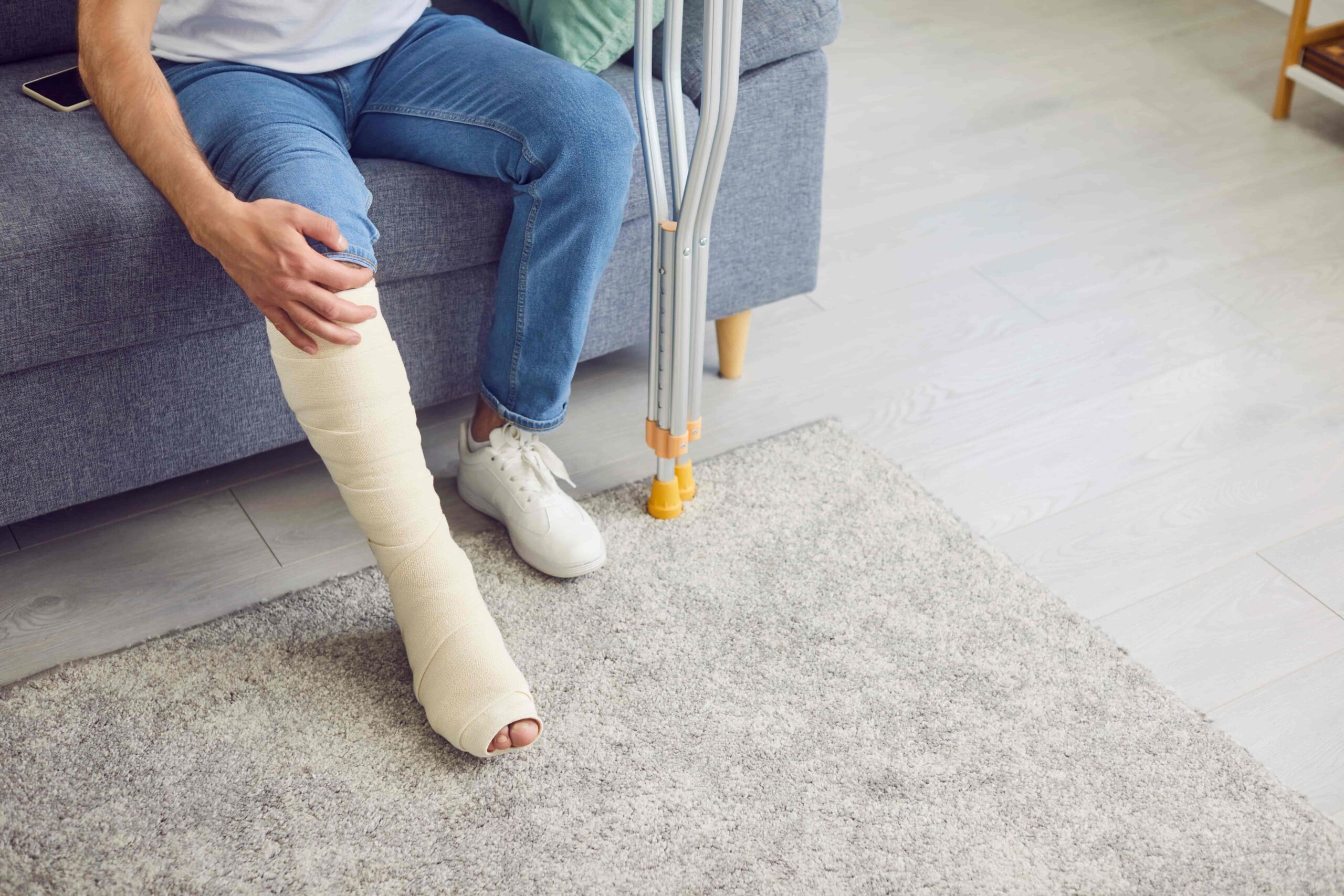 Injured person sitting on a couch with a broken leg in a cast and crutches at home