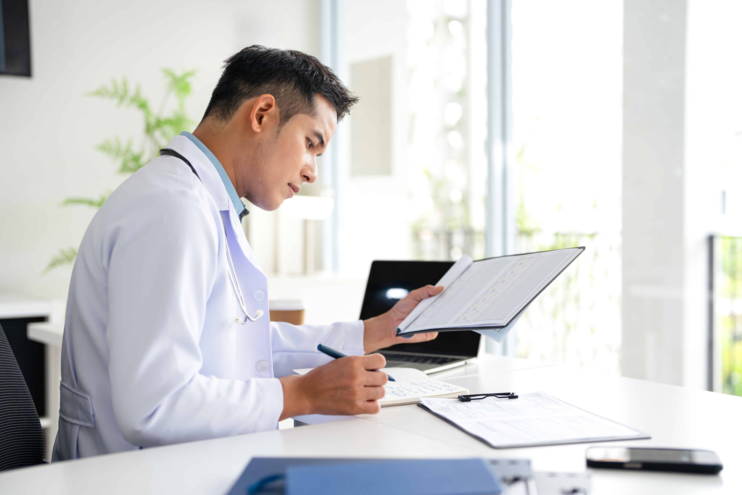 Doctor reviewing patient medical records and notes during clinical evaluation in a medical office.